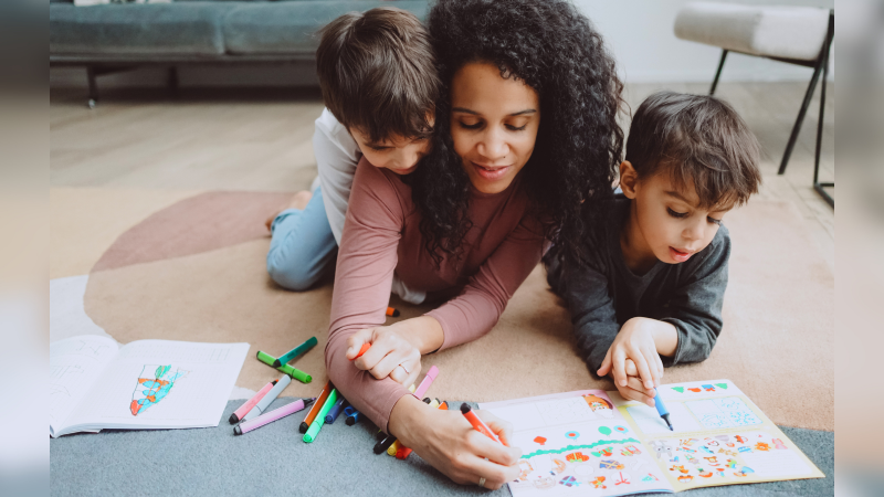 Duas crianças pintando e abraçando mulher