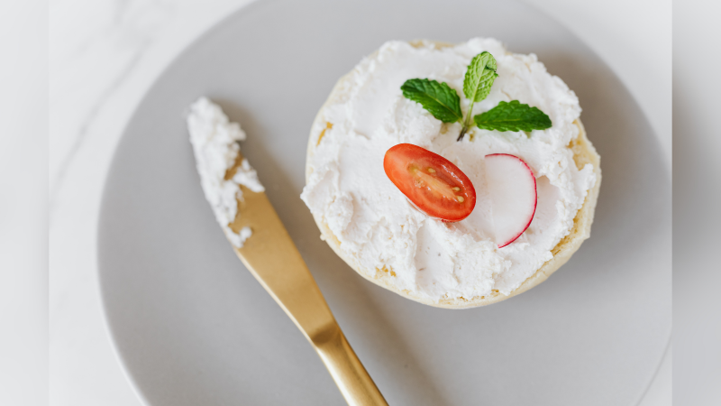 Imagem de queijo cottage com tomate cereja nele e faca com algo branco