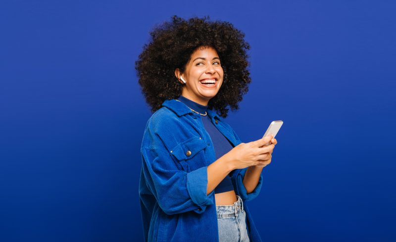 Mulher com cabelo encaracolado desfrutando de alguma música em seu smartphone na Semana do Consumidor