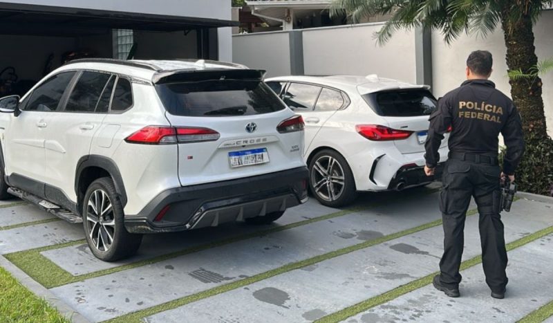 Traficante espanhol procurado pela Interpol é preso, foto mostra policial federal fardado em frente a carros e casa