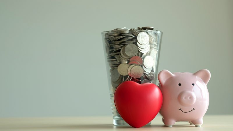Imagem de porquinho ao lado de coração e com copo cheio de moedas