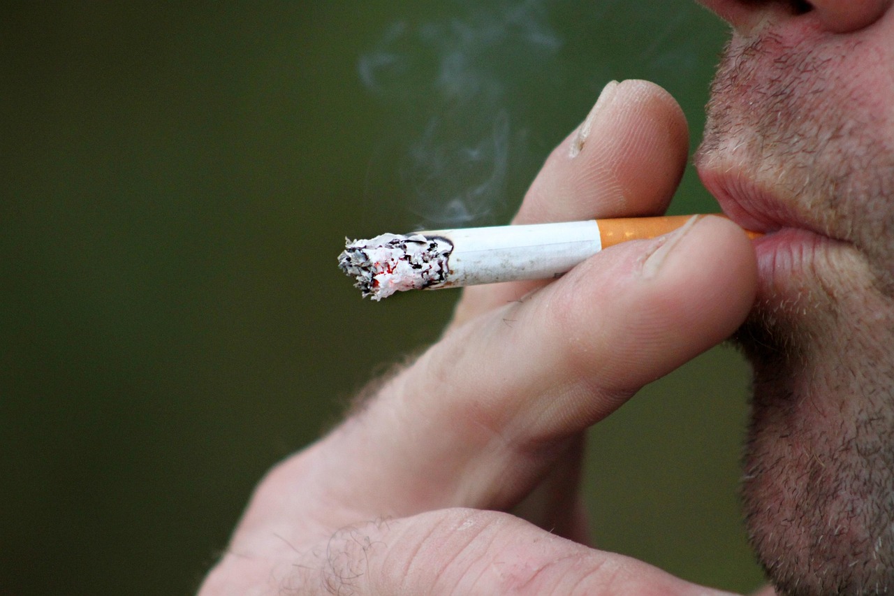 Close em um cigarro de filtro vermelho sendo fumado por um homem branco. A imagem ilustra matéria "‘Imposto do pecado’: entenda trecho polêmico da reforma tributária".