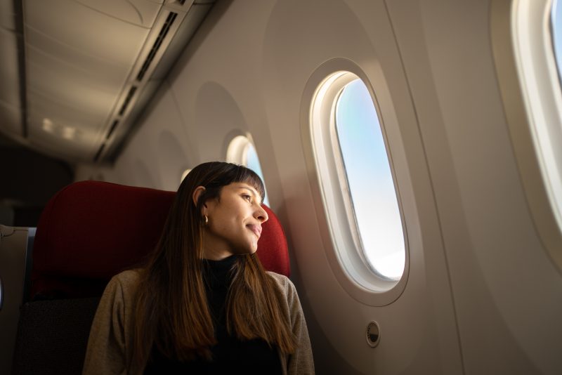 Viagem de avião Mulher sentada numa poltrona dentro do avião olhando pela janela