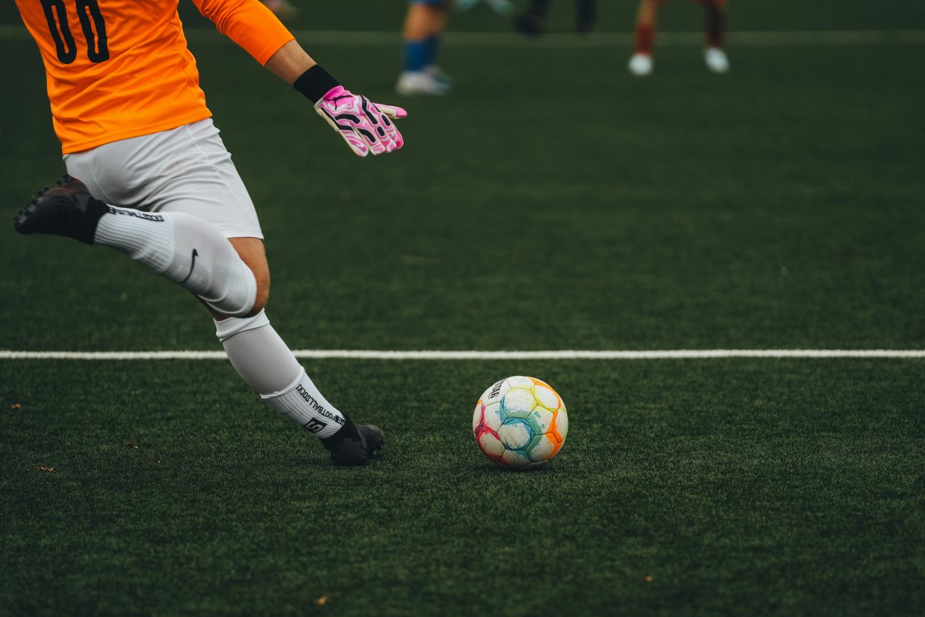 Jogador de futebol chutando uma bola em campo. Como funcionam as apostas esportivas online