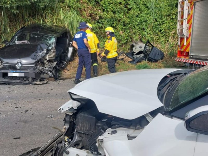Grave acidente em Blumenau Imagem mostra dois carros batidos e parados no trânsito. Um deles é branco e outro preto. Ambos estão com a frente detonada. Há também três pessoas na foto, sendo dois bombeiros e um guarda de trânsito que atenderam ao grave acidente