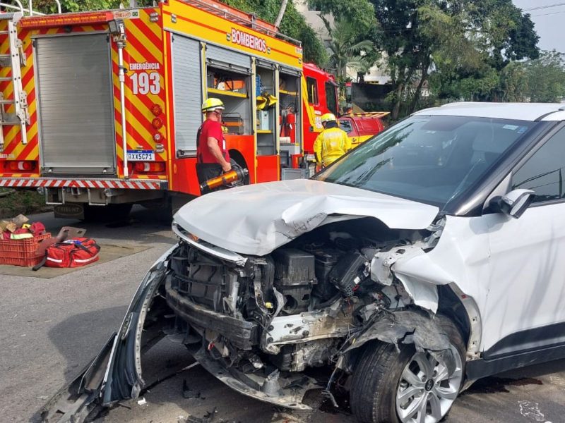 Grave acidente em Blumenau Imagem mostra um carro branco com a frente detonada após uma grave batida. Além disso, também há bombeiros na imagem, com a viatura