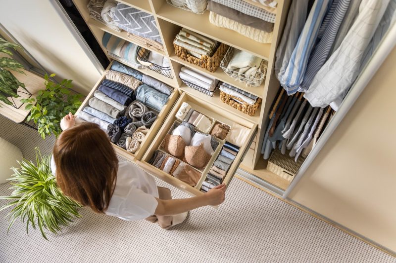 Dicas para dobrar roupas e economizar espaço no armário Jovem escolhendo qual sutiã usar enquanto está em frente a um guarda-roupa bem organizado para representar o conceito de dicas para dobrar roupas e economizar espaço no armário