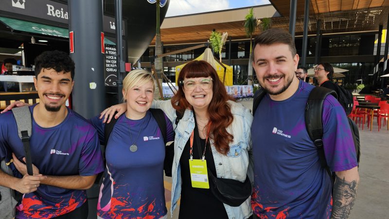 Dois homens e duas mulheres abraçados posando juntos para a foto, vestindo a camiseta oficial da Gamescom 2025