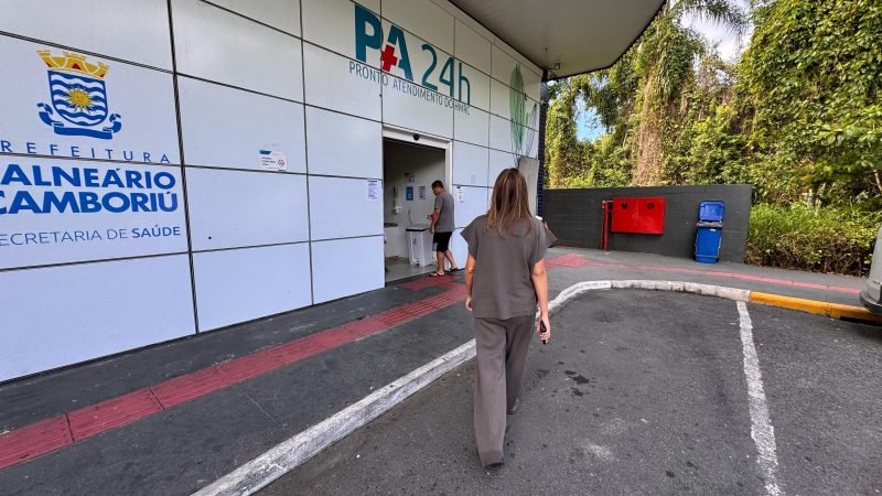 Hospital Ruth Cardoso Imagem mostra uma fachada de hospital escrito 'Balneário Camboriú' e também 'PA 24h'. Na frente dela também há uma mulher de costas caminhando em direção ao hospital