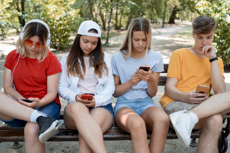 na foto aparecem quatro adolescentes que mexem no celular na hora do intervalo
