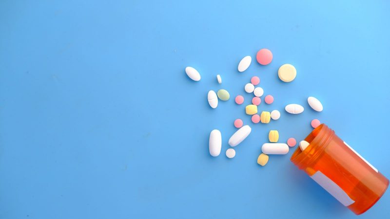 Tadalafila Imagem mostra um pote de remédio laranja transparente despejando vários comprimidos em uma base da cor azul para ilustrar a matéria que fala do medicamento tadalafila.