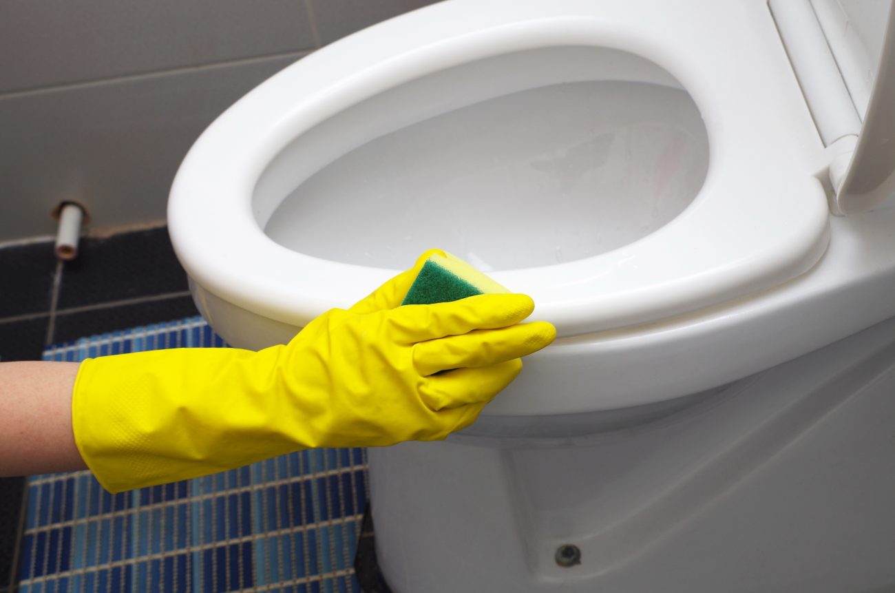 Limpeza do vaso sanitário Pessoa limpando a área externa do vaso sanitário para ilustrar como limpar a parte de baixo do vaso sanitário