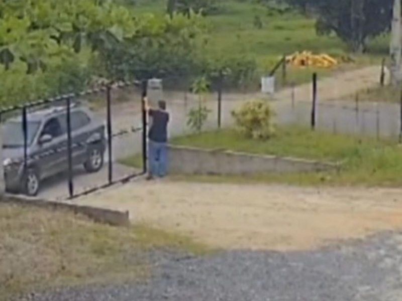 Empresário foi baleado em Gaspar Imagem mostra um homem de camisa preta perto de um portão. Do outro lado, há um carro preto. O terreno não tem pavimentação, mas conta com brita e grama. Empresário foi baleado em frente à empresa, mas sobreviveu ao ataque em Gaspar