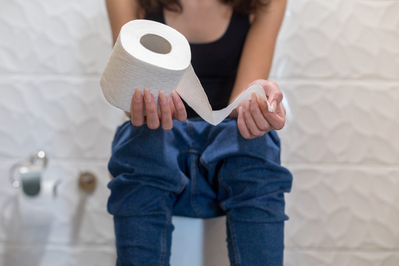 Mulher com papel higiênico Mulher sentada no vaso sanitário segurando rolo de papel higiênico