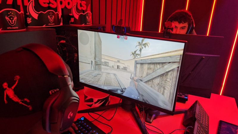 Dois homens sentados em frente aos seus computadores, jogando vídeo game, com fones nos ouvidos