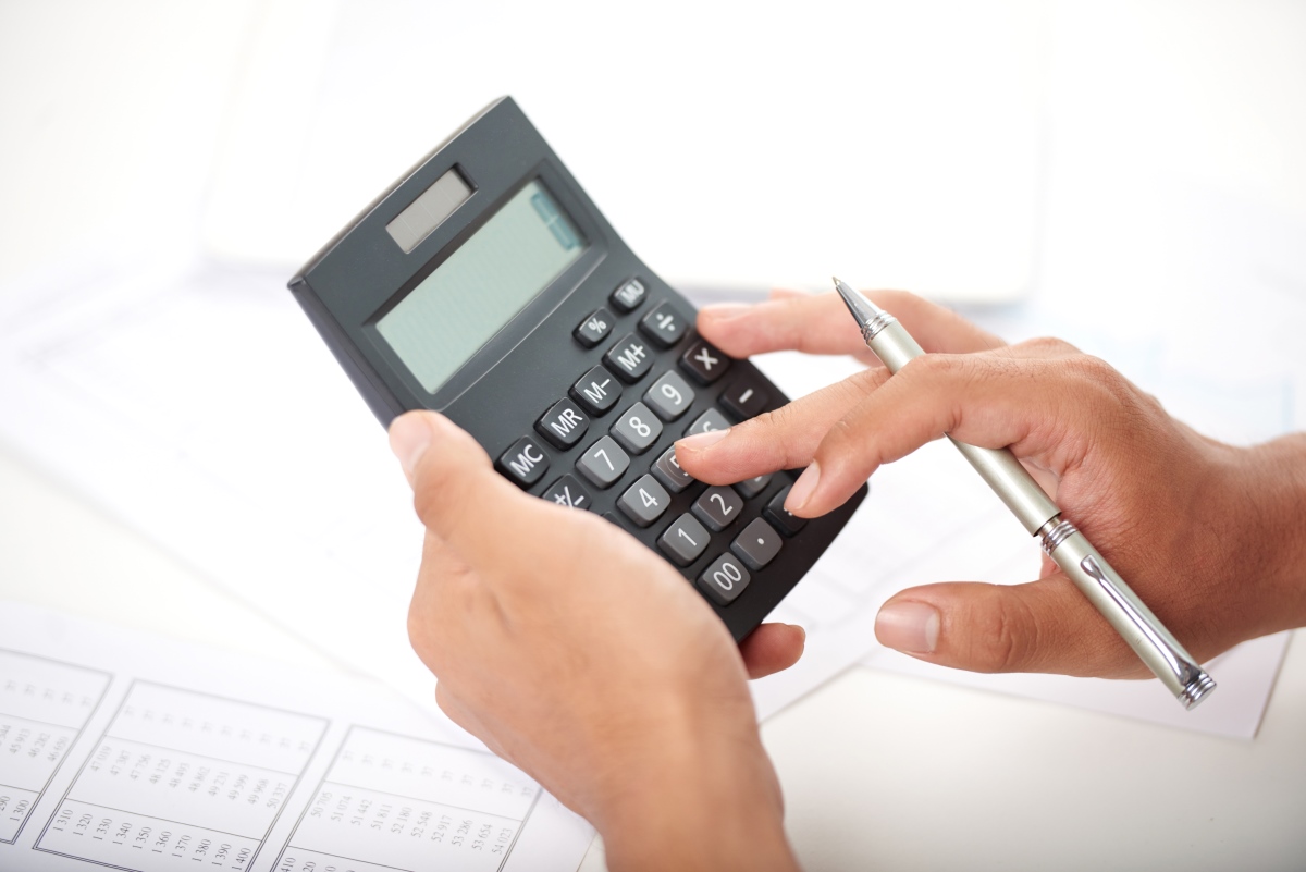 Mão segura uma calculadora e uma caneta. Imagem ilustra matéria "O que é reforma tributária? Veja o significado e por que ela é tão debatida no Brasil".