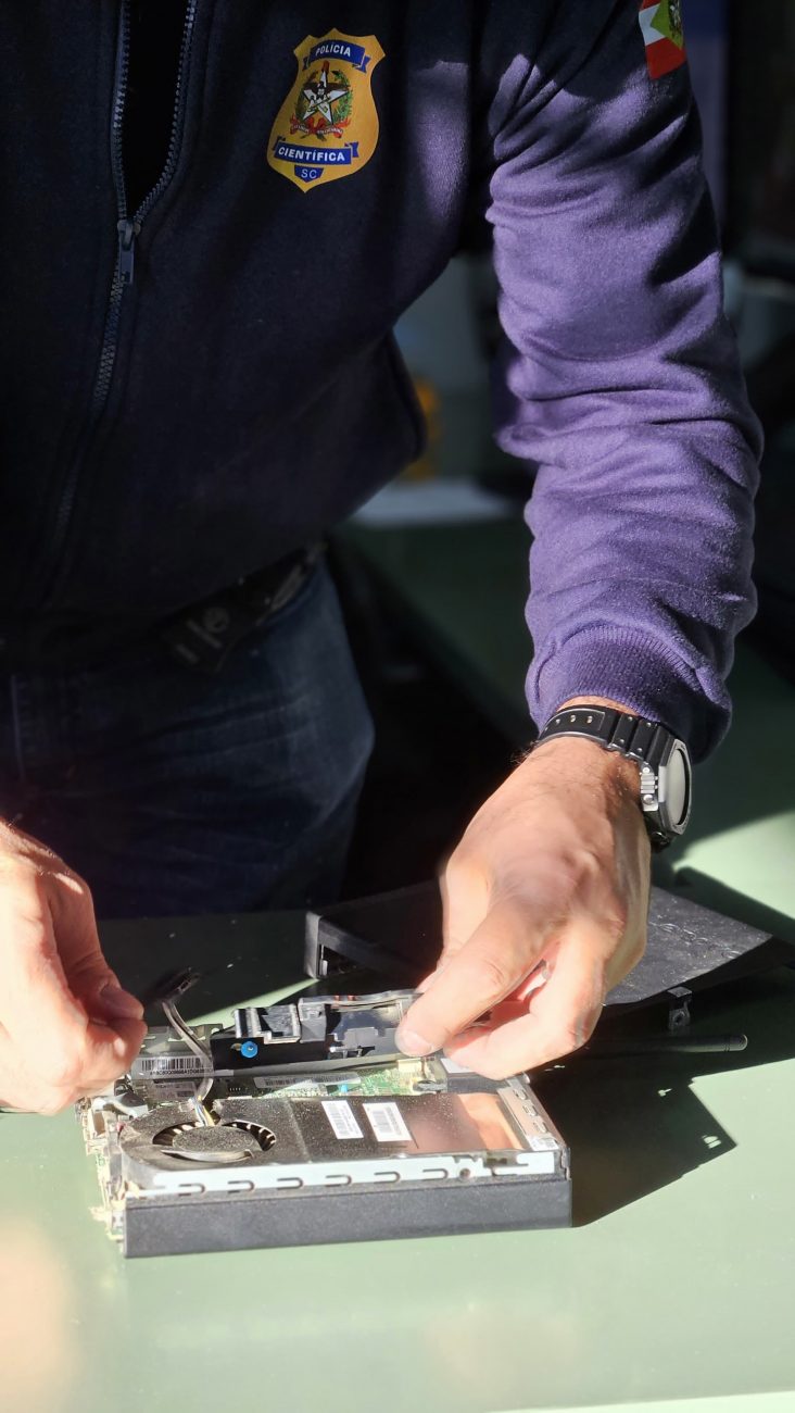 Foto mostra agente da Polícia Científica com aparelho eletrônico apreendido