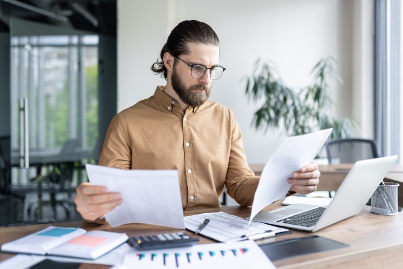 Como organizar documentos em casa Homem com notebook, documentos na mesa e calculadora para ilustrar como organizar documentos em casa