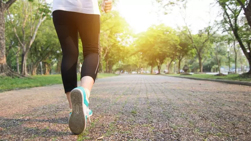 Caminhada traz vários benefícios Imagem de trás de uma pessoa caminhando em uma pista num parque para ilustrar a matéria sobre correr ou caminhar.