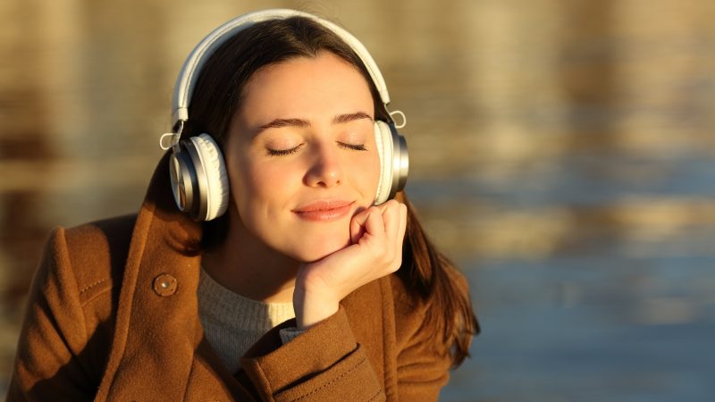 Pessoa de fone ouvindo música Pessoa usando jaqueta marrom de fone branco ouvindo música