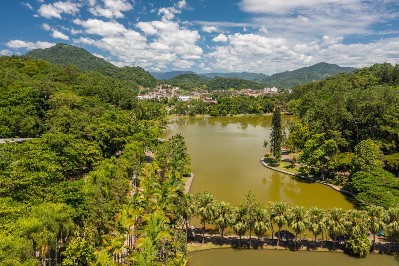 Parque Malwee Jaraguá do Sul Foto aérea do Parque Malwee, em Jaraguá do Sul. No centro da foto, um grande lago e ao redor dele muita vegetação. No horizonte aparecem morros e montanhas. O céu está azul com algumas nuvens.