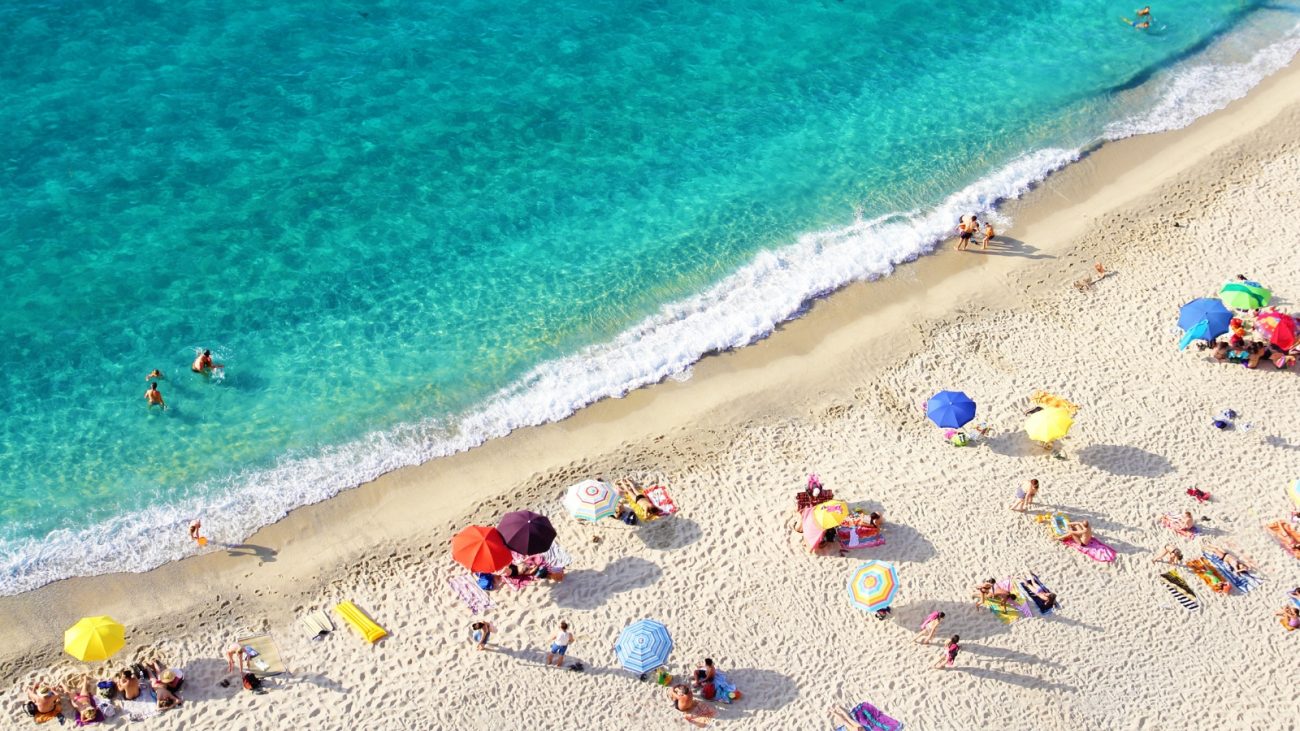 Pessoas em praia Pessoas em praia com guarda-chuva e mar cristalino