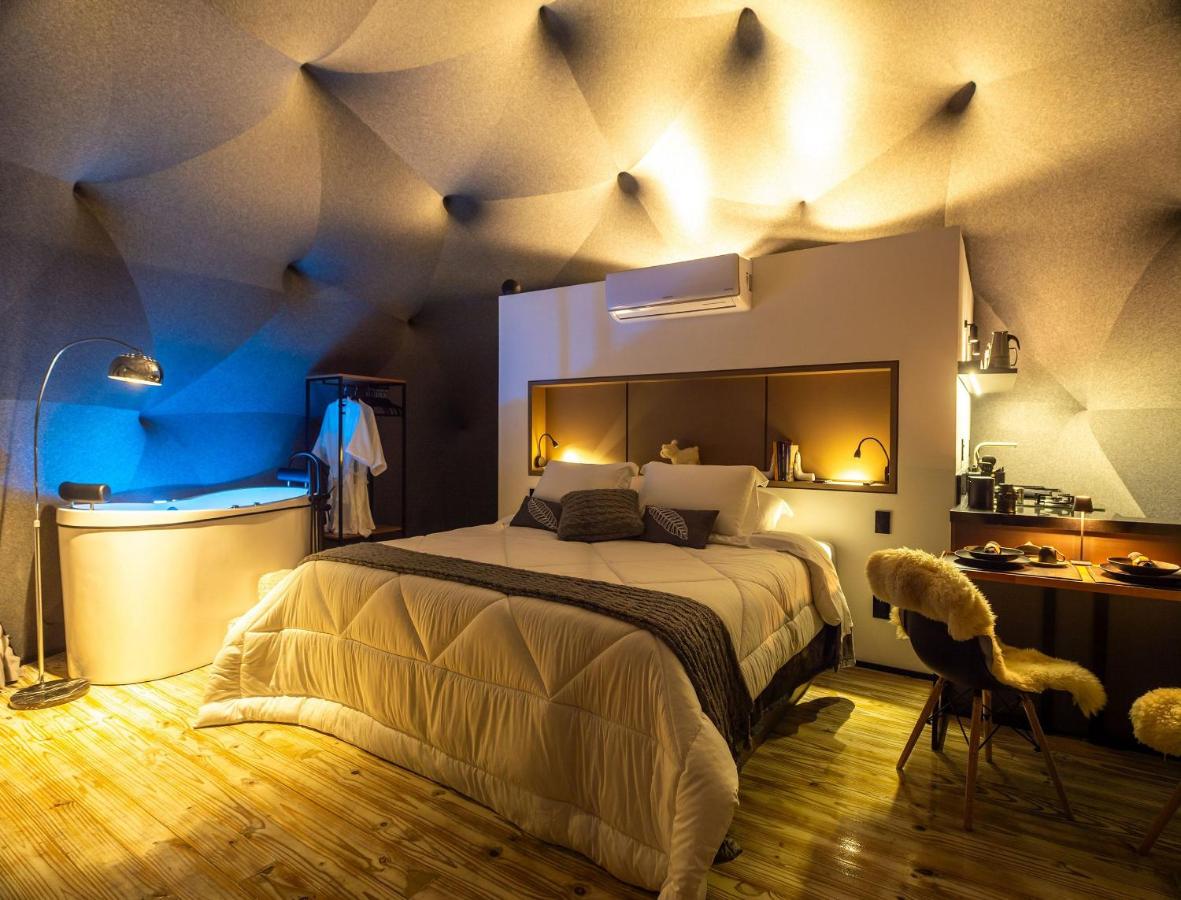 Kairos Glamping, em Rancho Queimado Imagem interna de frente pra uma cama de casal com banheira ao lado e cozinha do outro