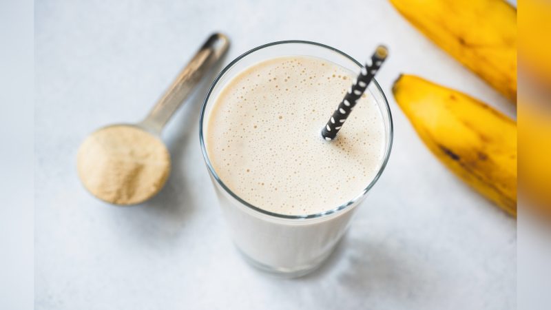 Vitamina de banana Copo com vitamina de banana, pó de banana e banana por trás