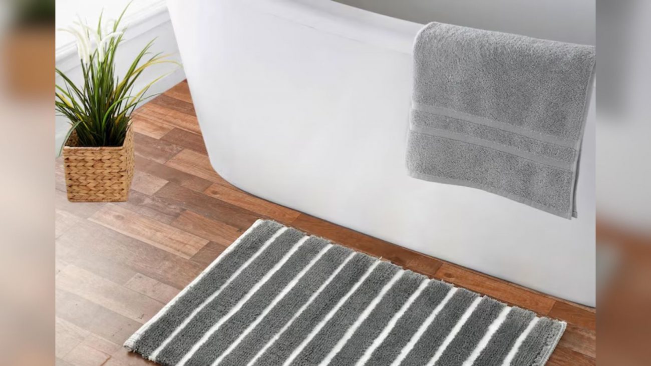 Imagem de uma banheira branca com uma toalha em cima com um vaso de plantas e um tapete no chão