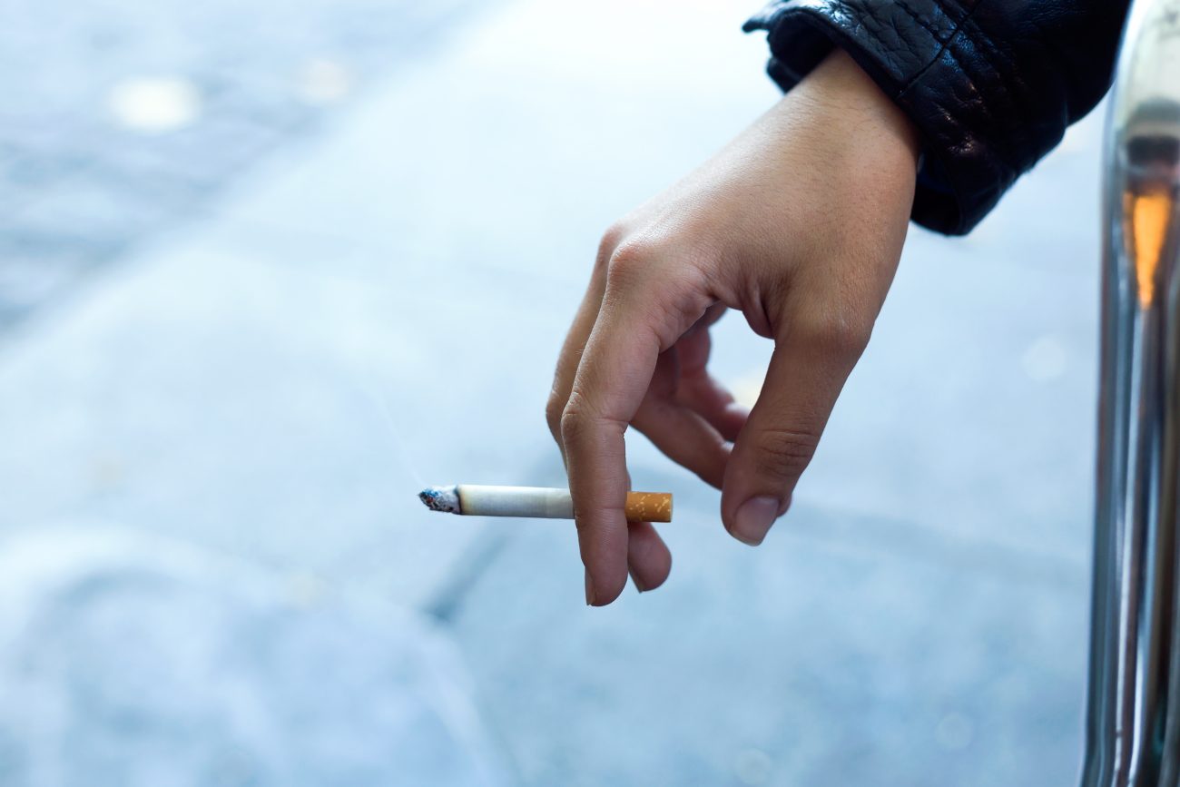 Pessoa com cigarro na mão em alusão à indústria do cigarro