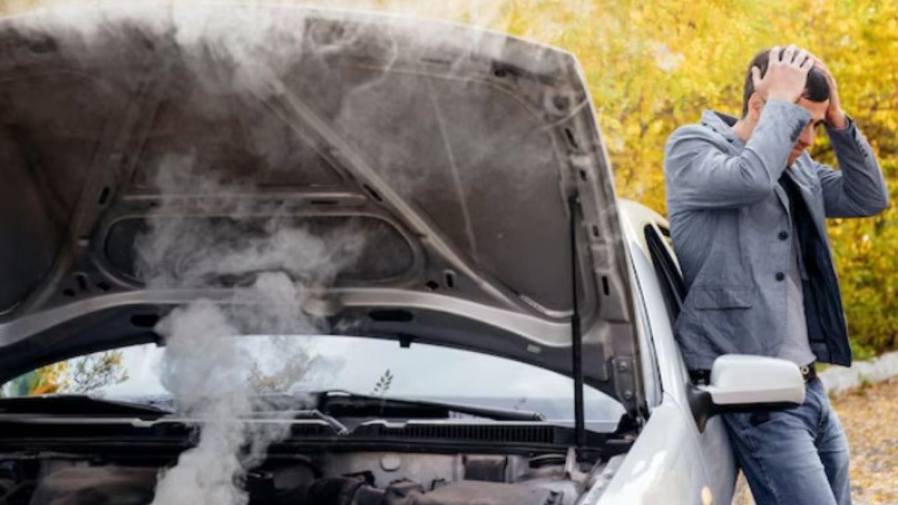 na foto aparece um homem com as mão na cabeça ao ver a bateria do carro soltando fumaça