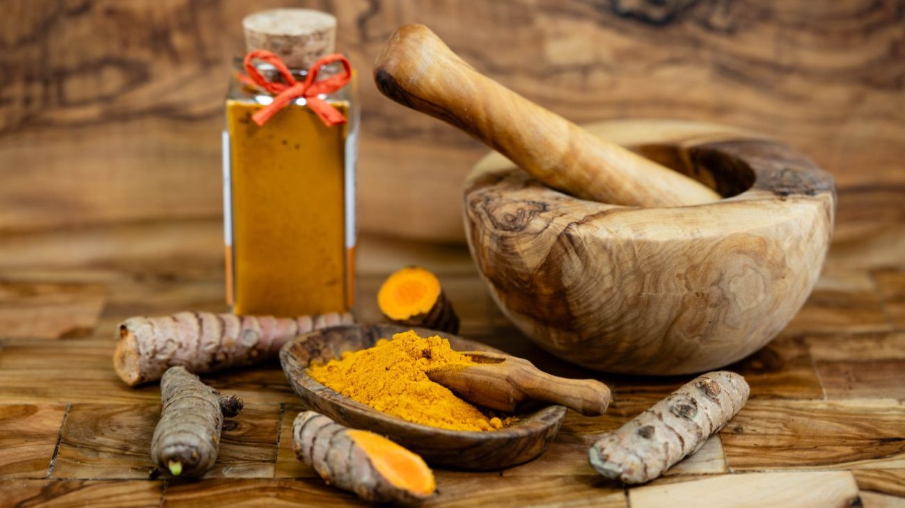 Imagem de especiarias em um ambiente rústico, incluindo cúrcuma em pó, gengibre fresco, e um pilão de madeira, ideal para preparações culinárias e remédios naturais.