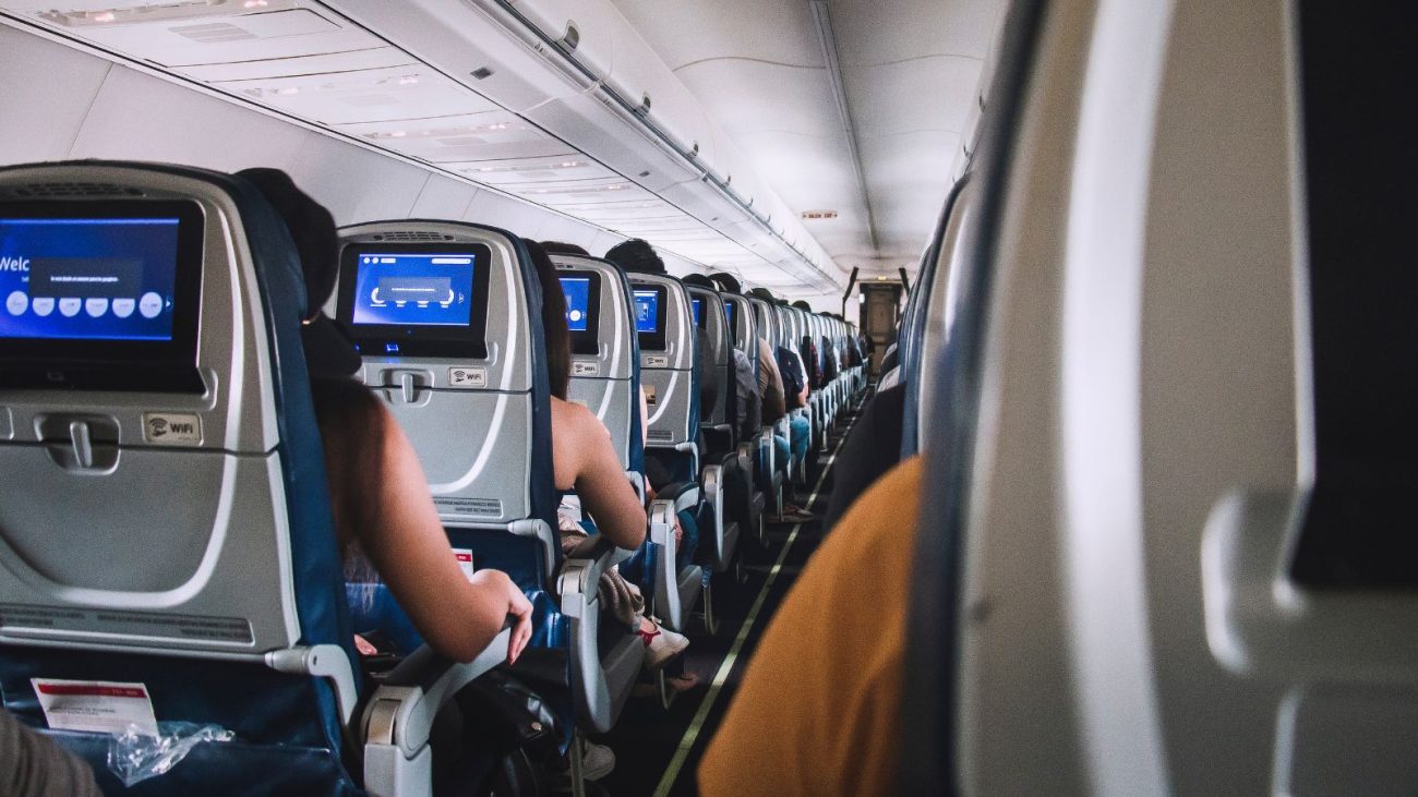 Interior de avião com passageiros sentados na classe econômica, ilustrando a busca pelo assento mais seguro no avião.