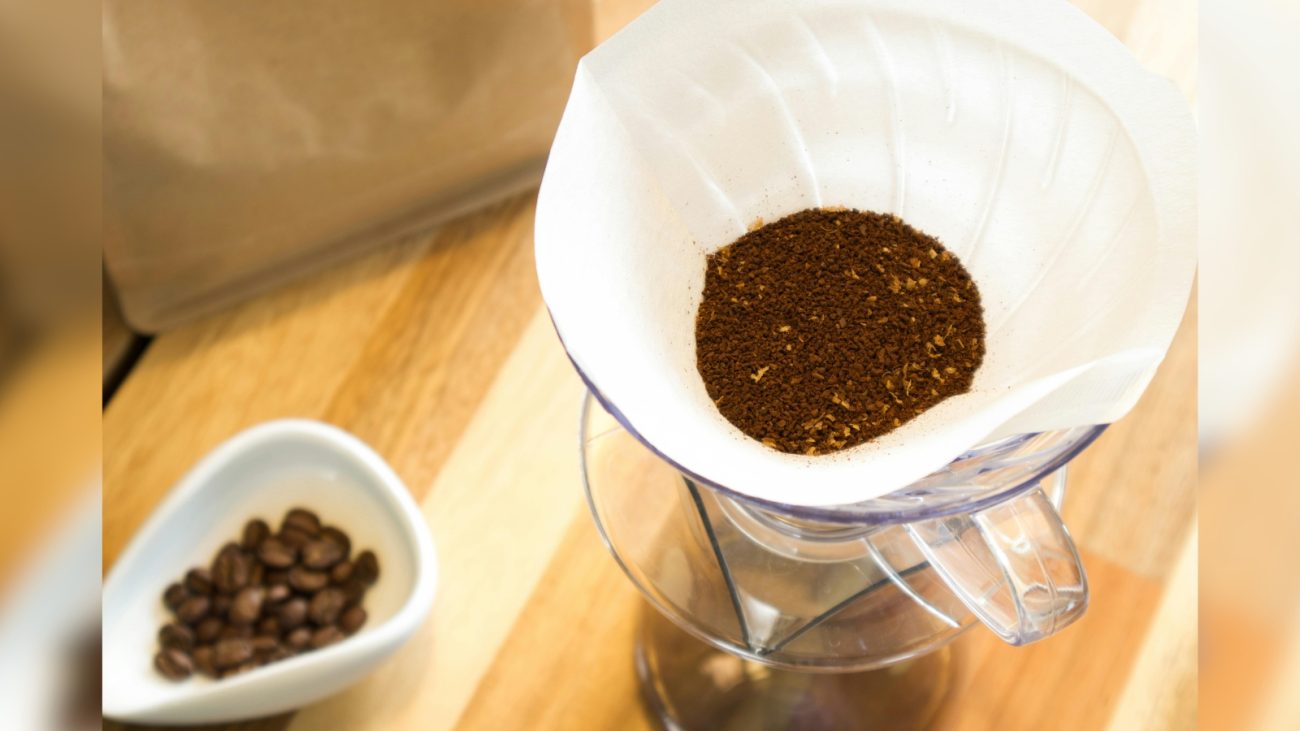 Preparo de café moído em filtro sobre panela de café com grãos de café ao lado, mostrando o processo de fazer café artesanal.