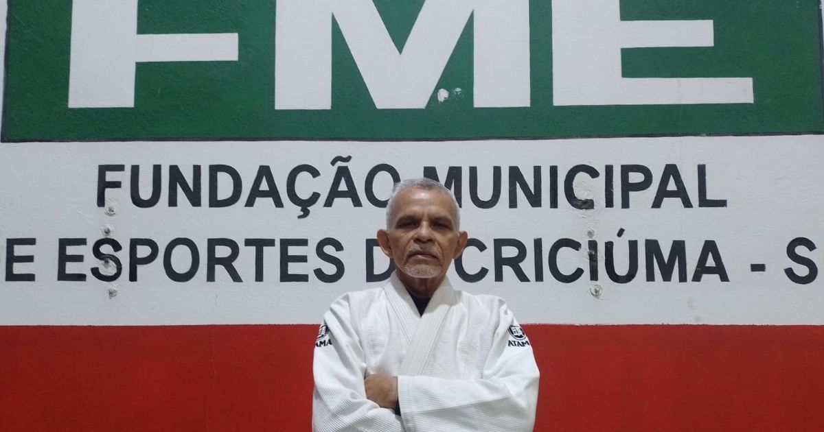 Imagem de um homem vestido com o uniforme de judô, na frente do letreiro da FMR, para fazer referência ao fato de que ele está estagiando na fundação 