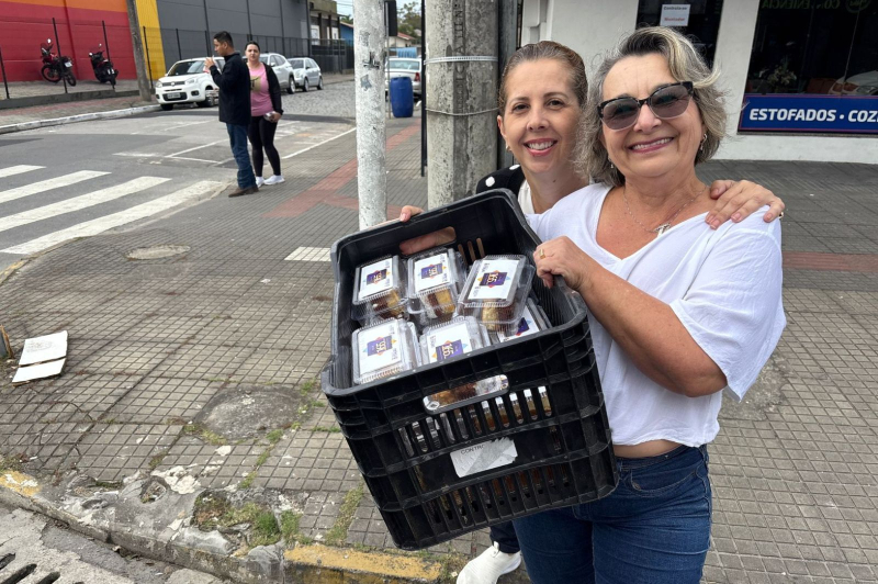 Duas mulheres segurando potes com fatias do bolo de aniversário de Itajaí
