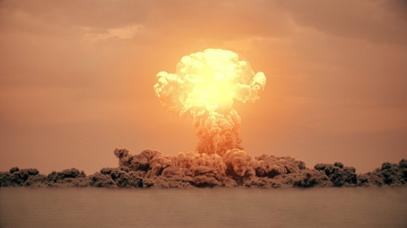 Explosão de bomba atômica formando uma grande nuvem de cogumelo iluminada em tons laranja e amarelo no céu, representando uma detonação nuclear