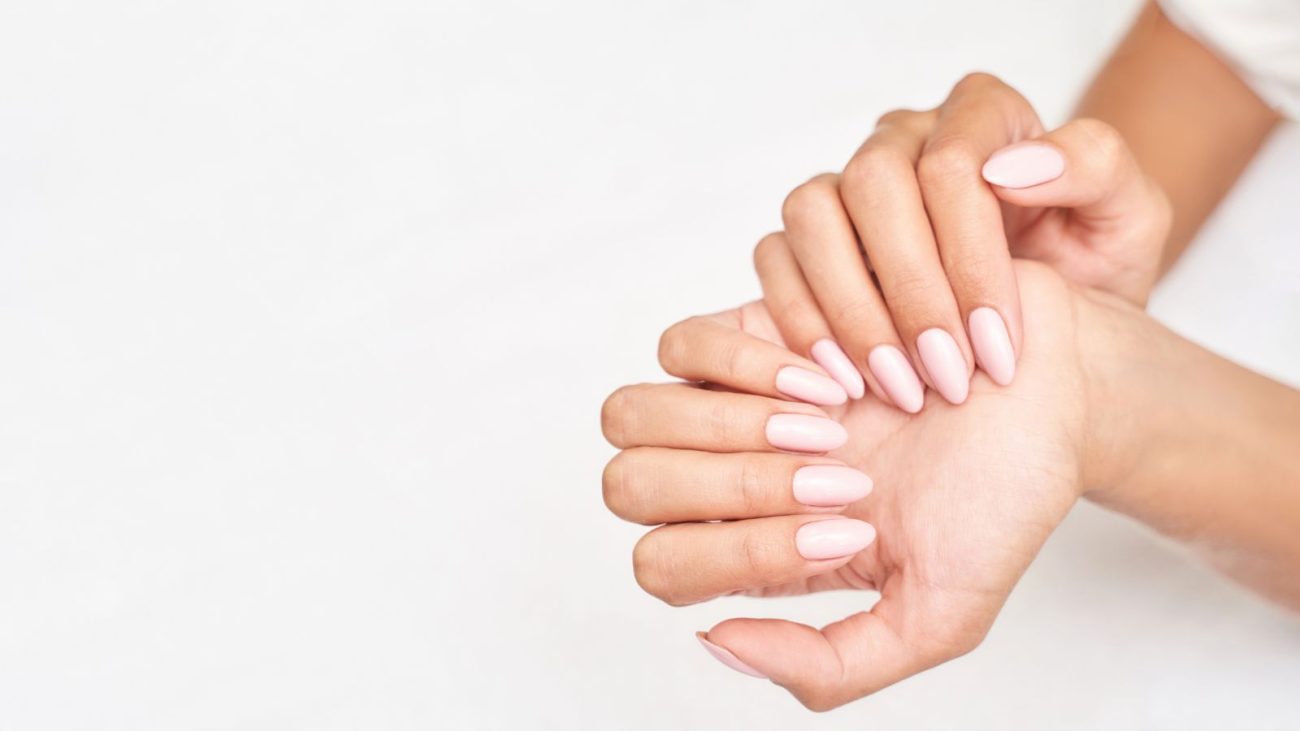 Imagem de unhas bem cuidadas e esmaltadas de cor rosa claro, simbolizando cuidados com as mãos e beleza.