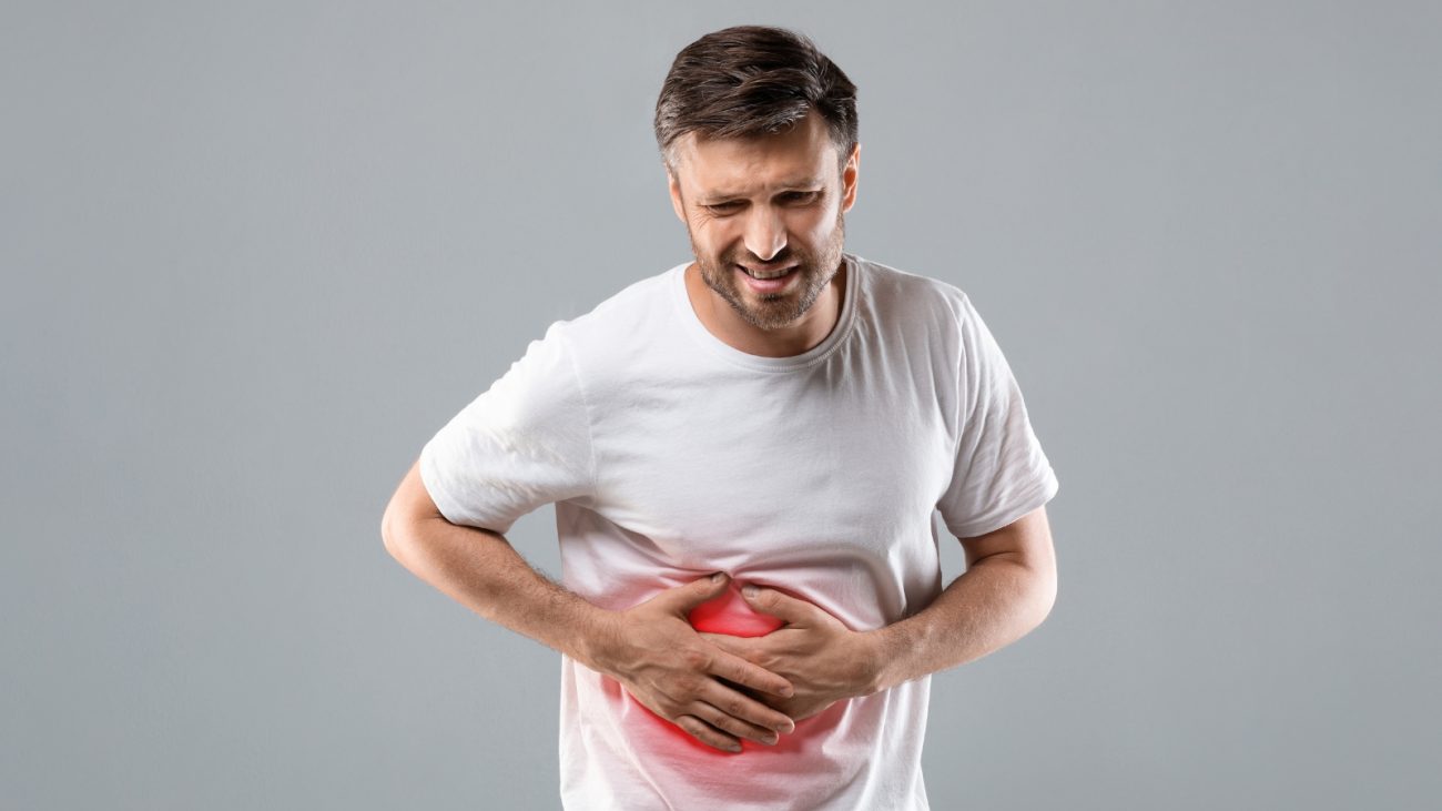 Homem com dor abdominal segurando o estômago, sinalizando desconforto ou dor de estômago, simbolizando problemas digestivos ou gastrite.