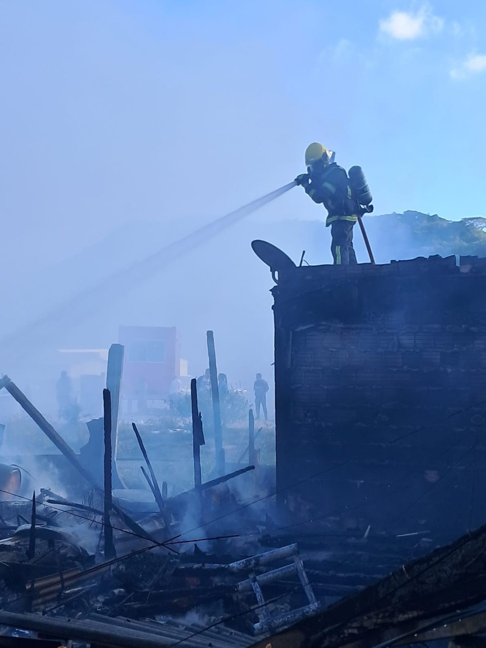 Foto mostra bombeiro com mangueira apagando fogo causado por incêndio