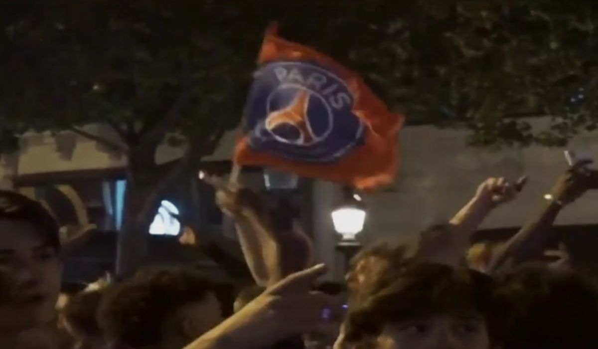PSG venceu a Liga dos Campeões, foto mostra pessoas comemorando enquanto uma segura uma bandeira do PSG
