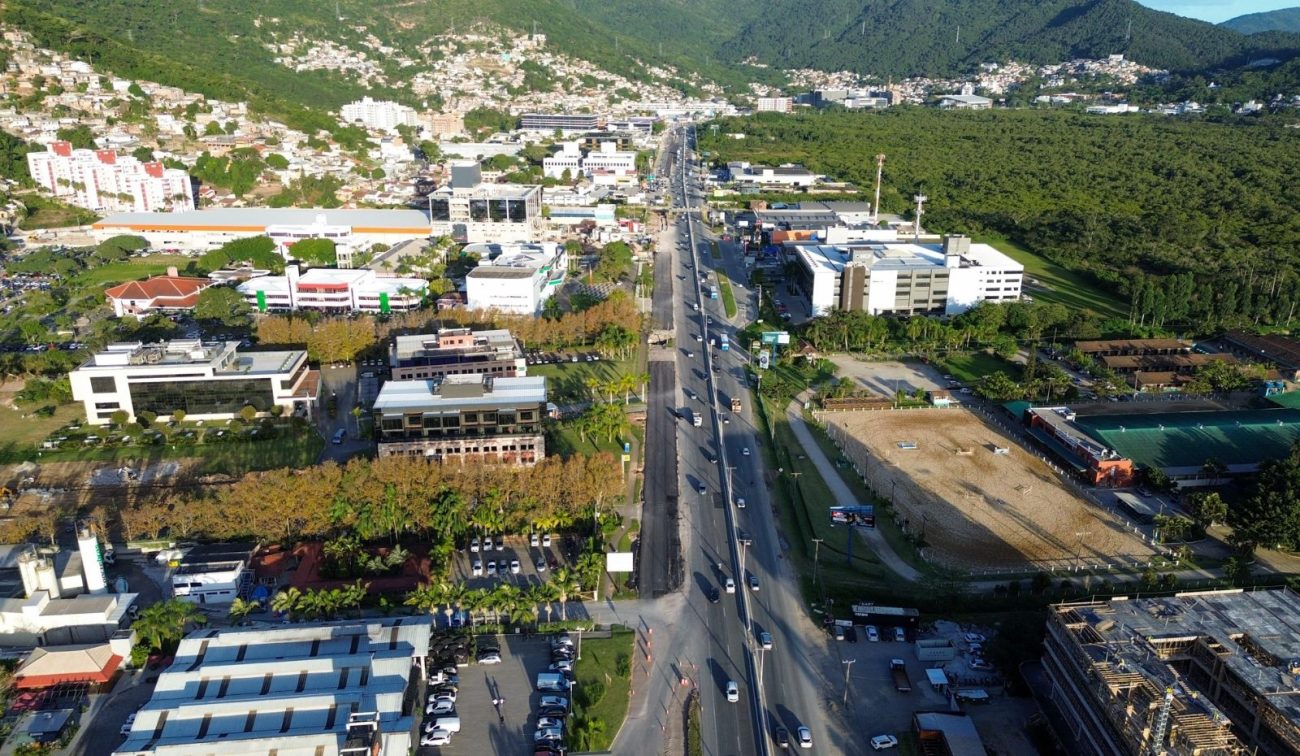 Painel do Governo de Santa Catarina destaca a obra da terceira faixa da SC-401 pelo Programa Estrada Boa, com parte do asfalto novo visível e carros circulando ao lado da pista em construção