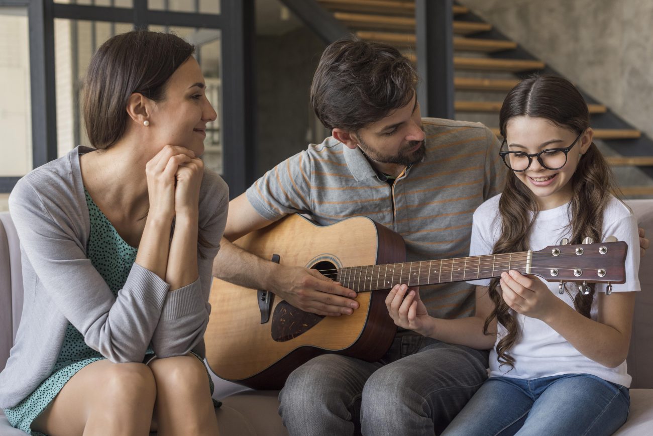 Pais tocando violão com a filha na sala de casa 