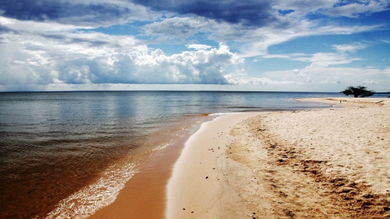 Praia paradisíaca de areia branca e água cristalina sob céu parcialmente nublado, ideal para relaxar e curtir a natureza.
