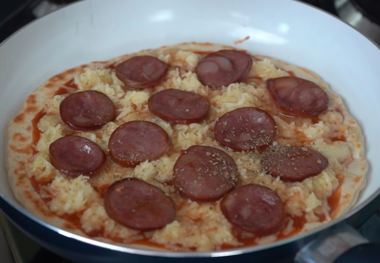 Orégano sendo despejado na pizza de frigideira quase pronta