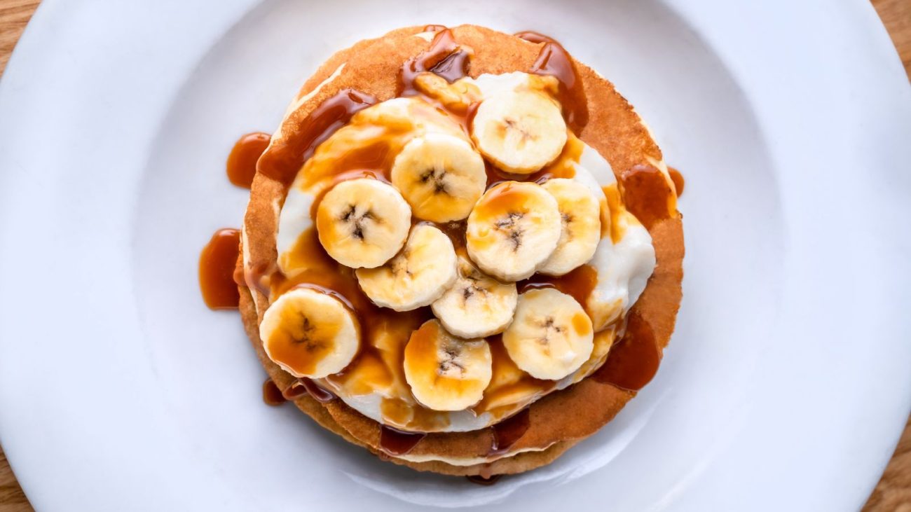 Panquecas sem farinha com bananas e calda de caramelo, servidas em prato branco. Uma deliciosa sobremesa.