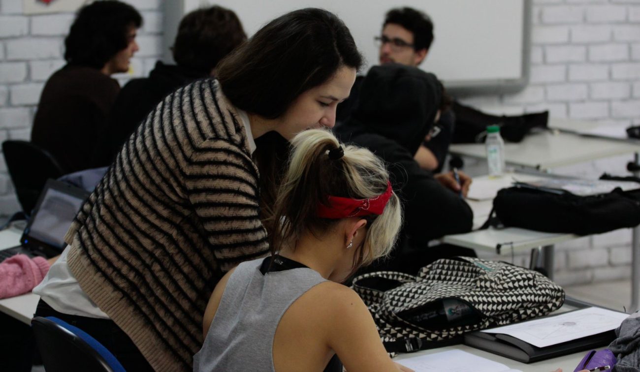 Professora auxilia aluna em sala de aula durante atividade acadêmica, representando o trabalho de professores substitutos no ensino superior