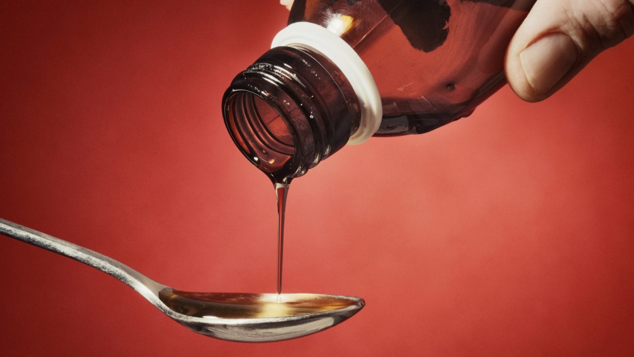 Imagem de um tubo de xarope de chocolate sendo despejado em uma colher, com fundo vermelho. Ideal para ilustrar doces e sobremesas com chocolate.