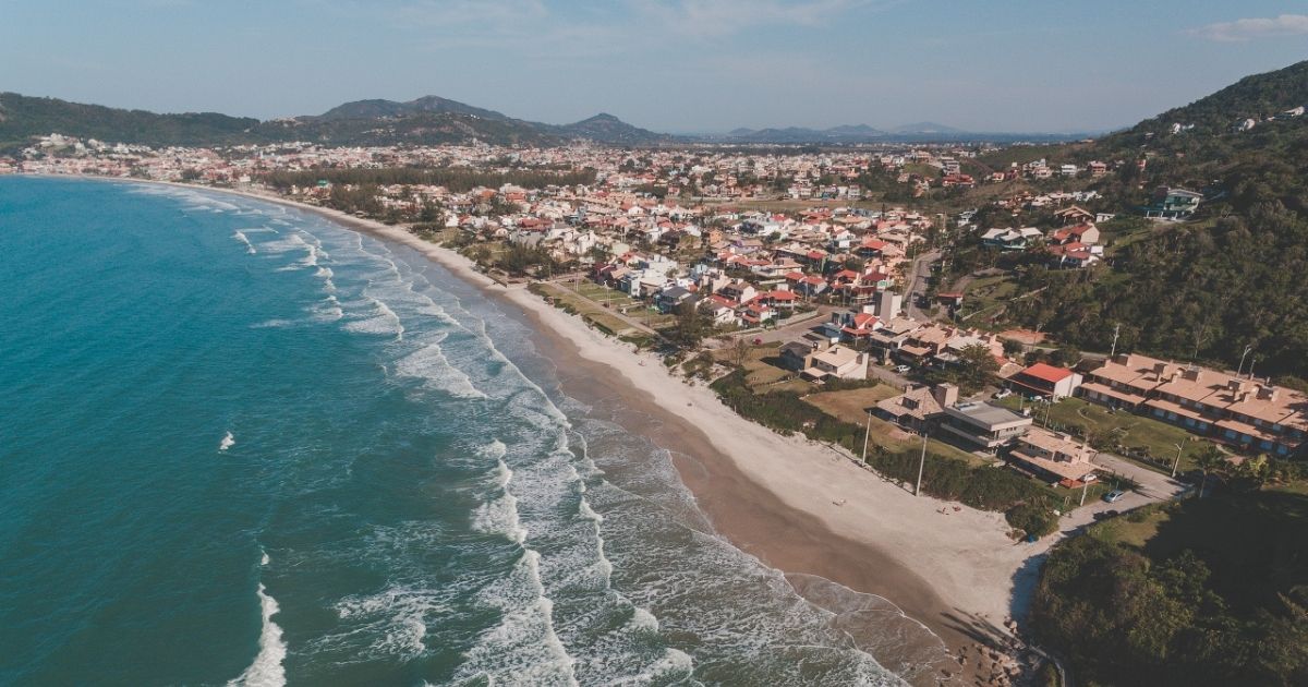 Imagem aérea de Garopaba, com vista para as casas e o litoral azul da cidade, para relacionar ao fato de que a festa de ano-novo no município será feito em quatro praias 