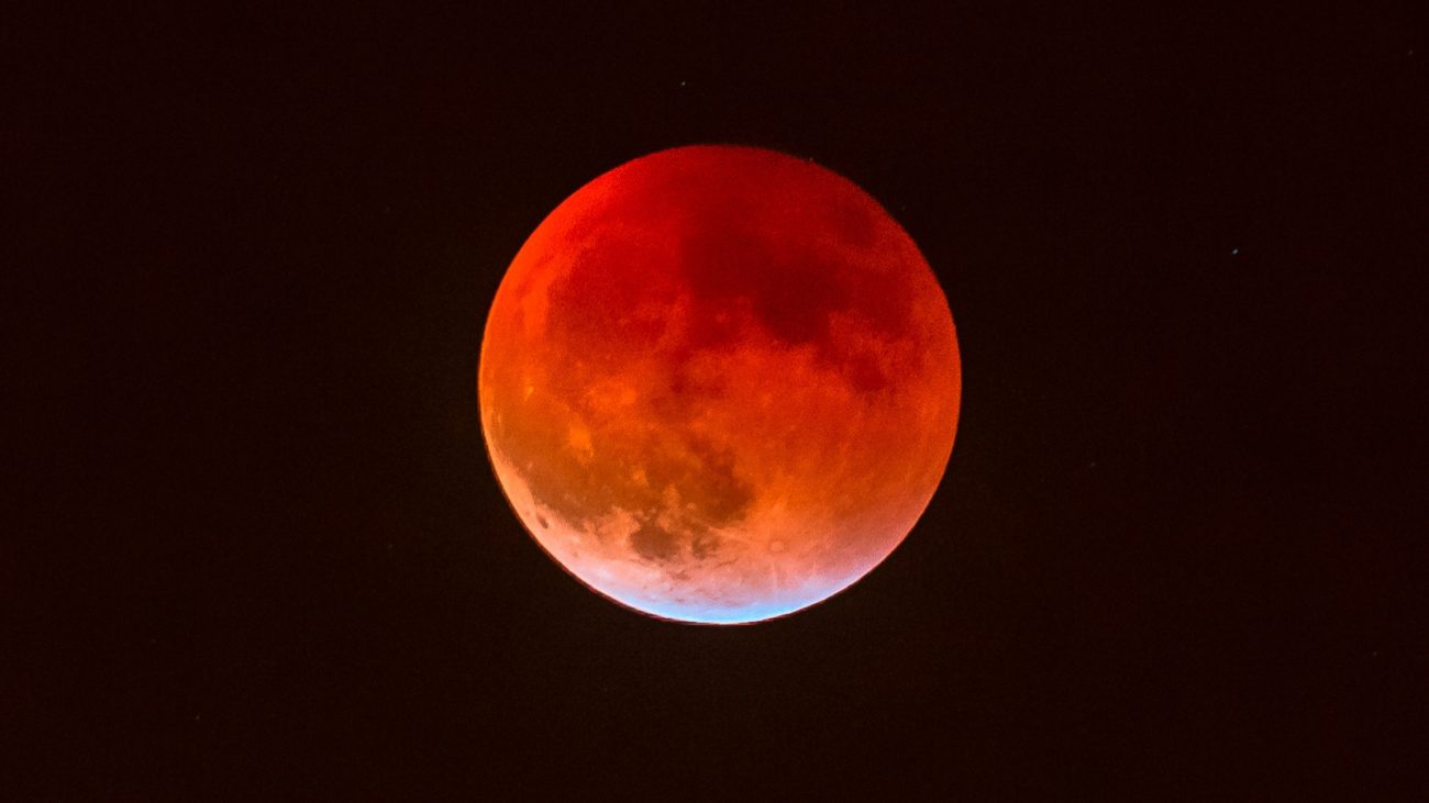Imagem de uma fase de eclipse lunar com tonalidades vermelhas, destacando a coloração avermelhada da lua durante o fenômeno astronômico.